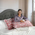 Woman sitting on a bed with decorative pillows and a gray headboard.