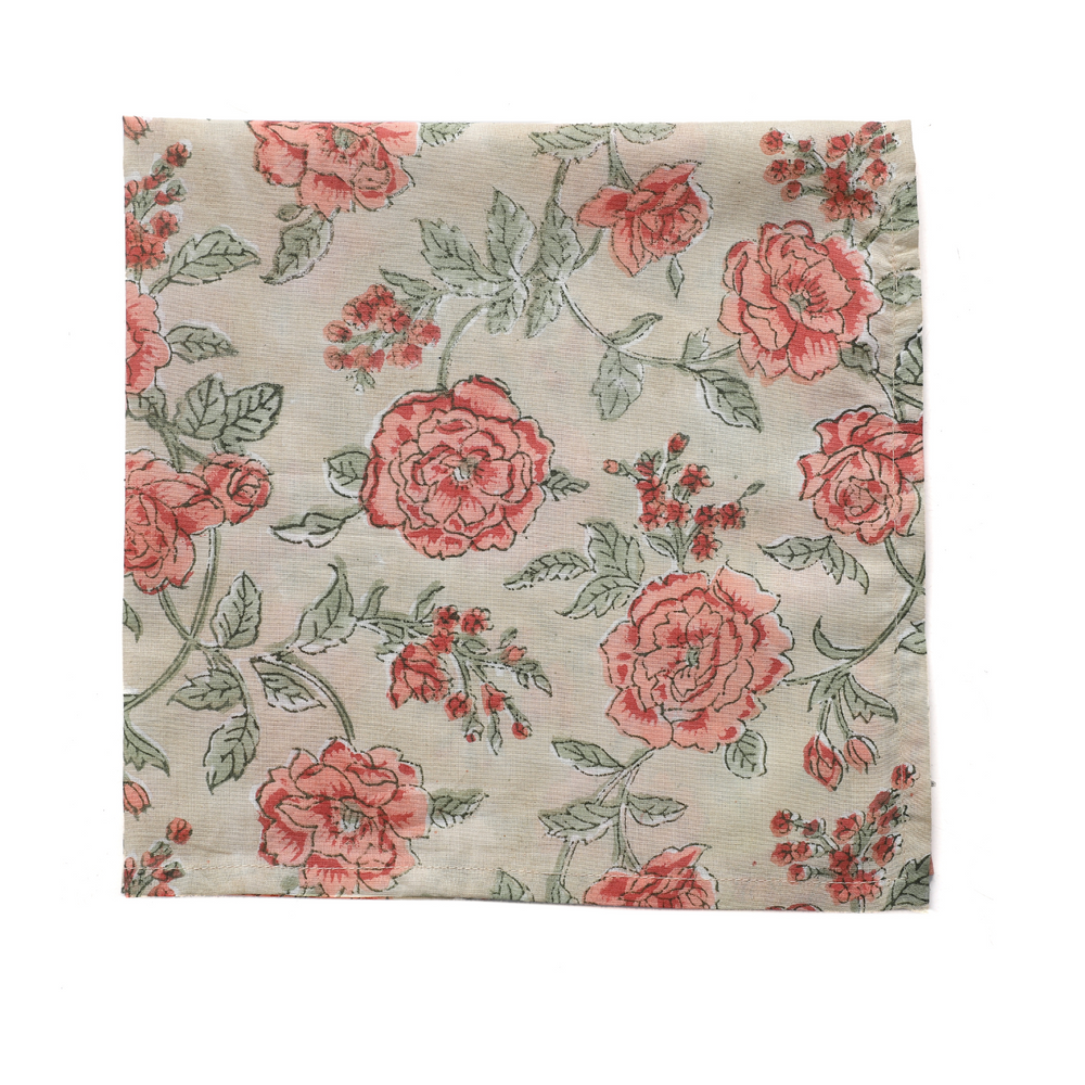 Single pink and tan floral napkin folded under silverware on a white plate.