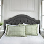 Green patterned pillows on a bed with a gray upholstered headboard in a bedroom setting.
