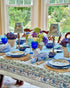 Poppy Blue Cotton Tablecloth on Farmhouse Table with dining table setup of plates, napkins, wine glasses, and placemats.