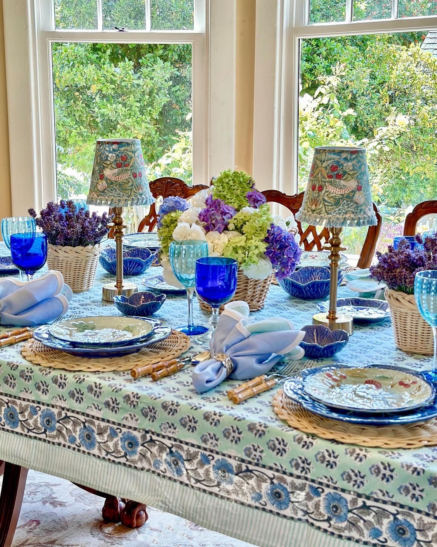 Poppy Blue Cotton Tablecloth on Farmhouse Table with dining table setup of plates, napkins, wine glasses, and placemats.