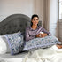 Woman sitting on a bed with decorative pillows and holding a mug.