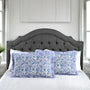 Decorative pillows with blue floral pattern on a bed with a tufted headboard.