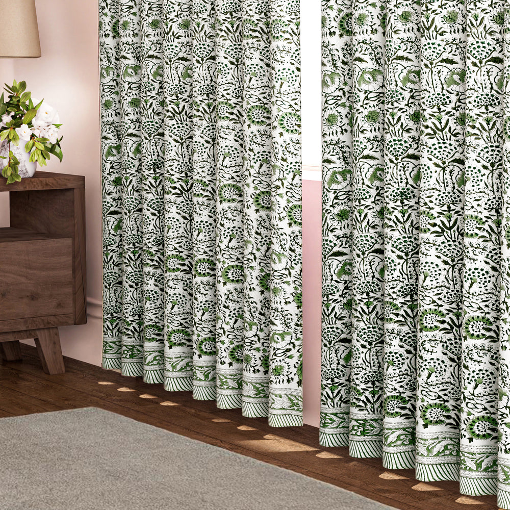 Semi-sheer cotton block print curtains in green, hanging in a room with a light filtering through, showcasing a boho-chic style.