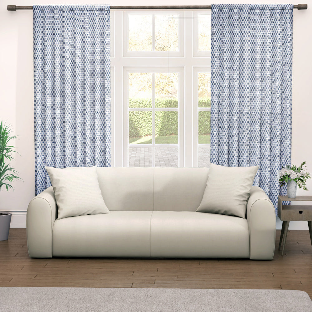 A pair of semi-sheer blue cotton block print curtains hanging in a room with a light coming through, showcasing a boho-chic design.