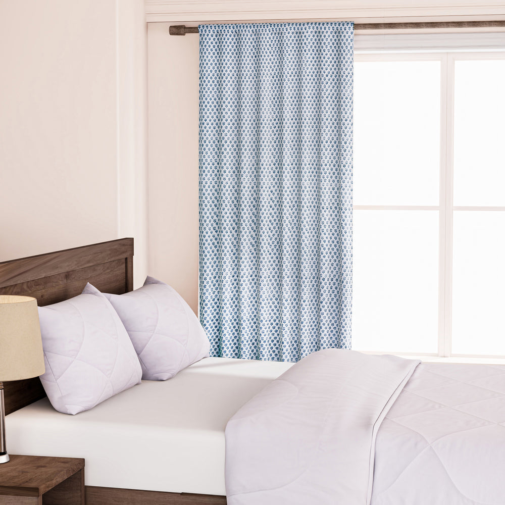 A pair of semi-sheer blue cotton block print curtains hanging in a room with a light coming through, showcasing a boho-chic design.