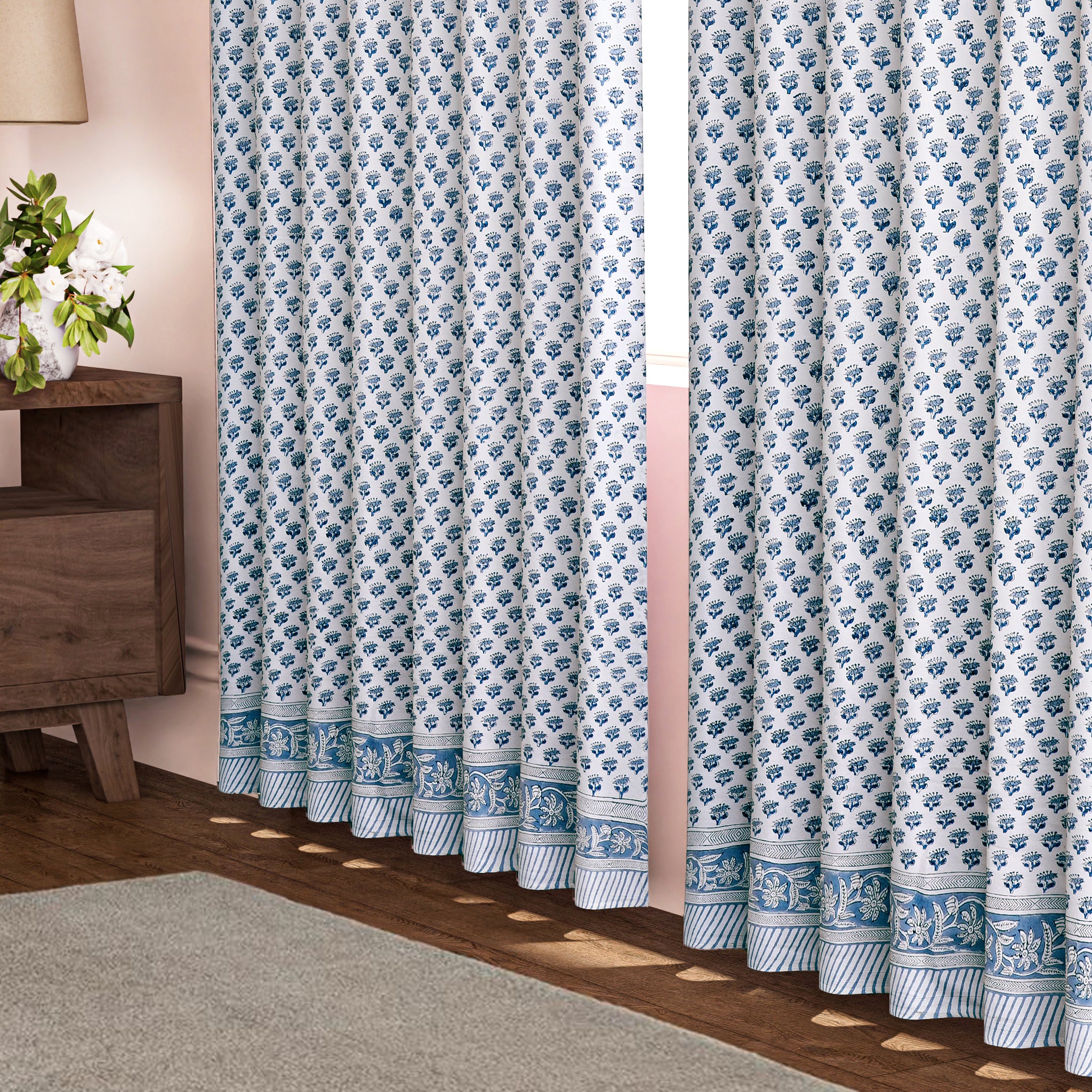 A pair of semi-sheer blue cotton block print curtains hanging in a room with a light coming through, showcasing a boho-chic design.