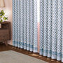 A pair of semi-sheer blue cotton block print curtains hanging in a room with a light coming through, showcasing a boho-chic design.