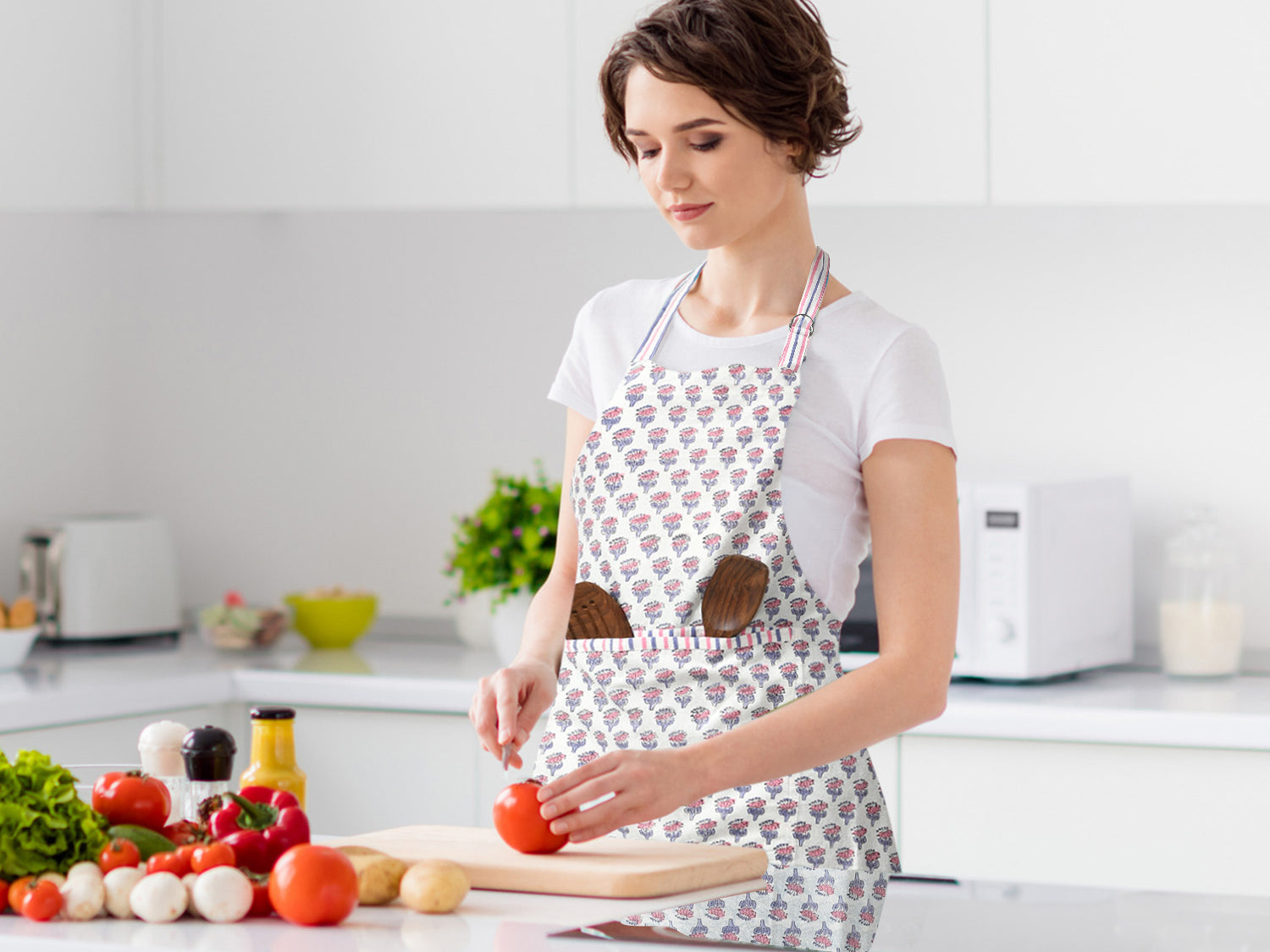 lady wearing a pink and white kitchen apron with wooden kitchen utensils in the front pocket while cutting vegetables on a cutting board