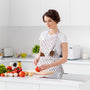 lady wearing a pink and white kitchen apron with wooden kitchen utensils in the front pocket while cutting vegetables on a cutting board