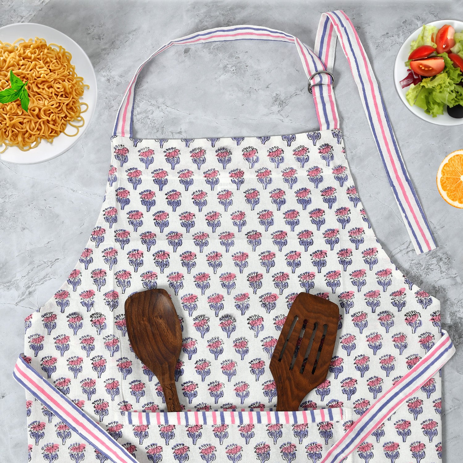 pink and white kitchen apron laying on the counter with wooden kitchen utensils in the front pocket