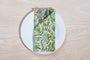 Single green floral napkin wrapped around silverware on a white plate.