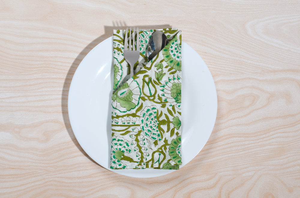 Single green floral napkin wrapped around silverware on a white plate.