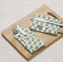green floral napkin placed under silverware on wooden serving tray, with matching napkins rolled beside.