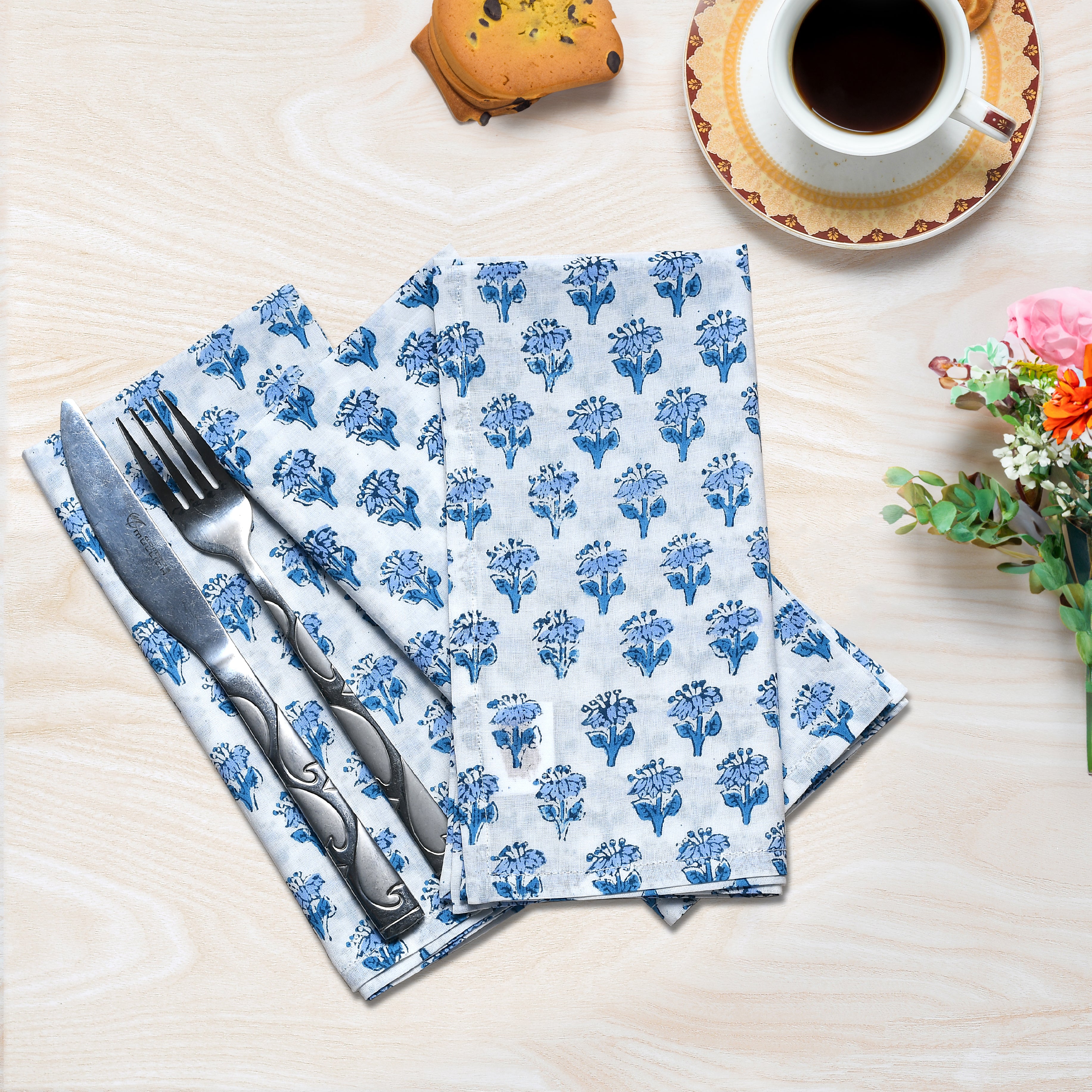 Flat lay of three folded blue floral napkins with one holding silverware.

