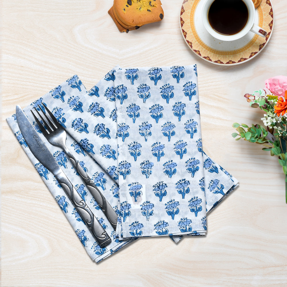 Flat lay of three folded blue floral napkins with one holding silverware.

