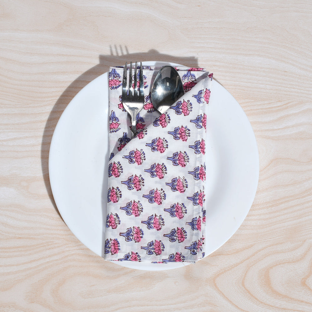 Single pink and white floral napkin folded under silverware on a white plate.
