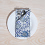 Single blue floral napkin wrapped around silverware on a white plate.

