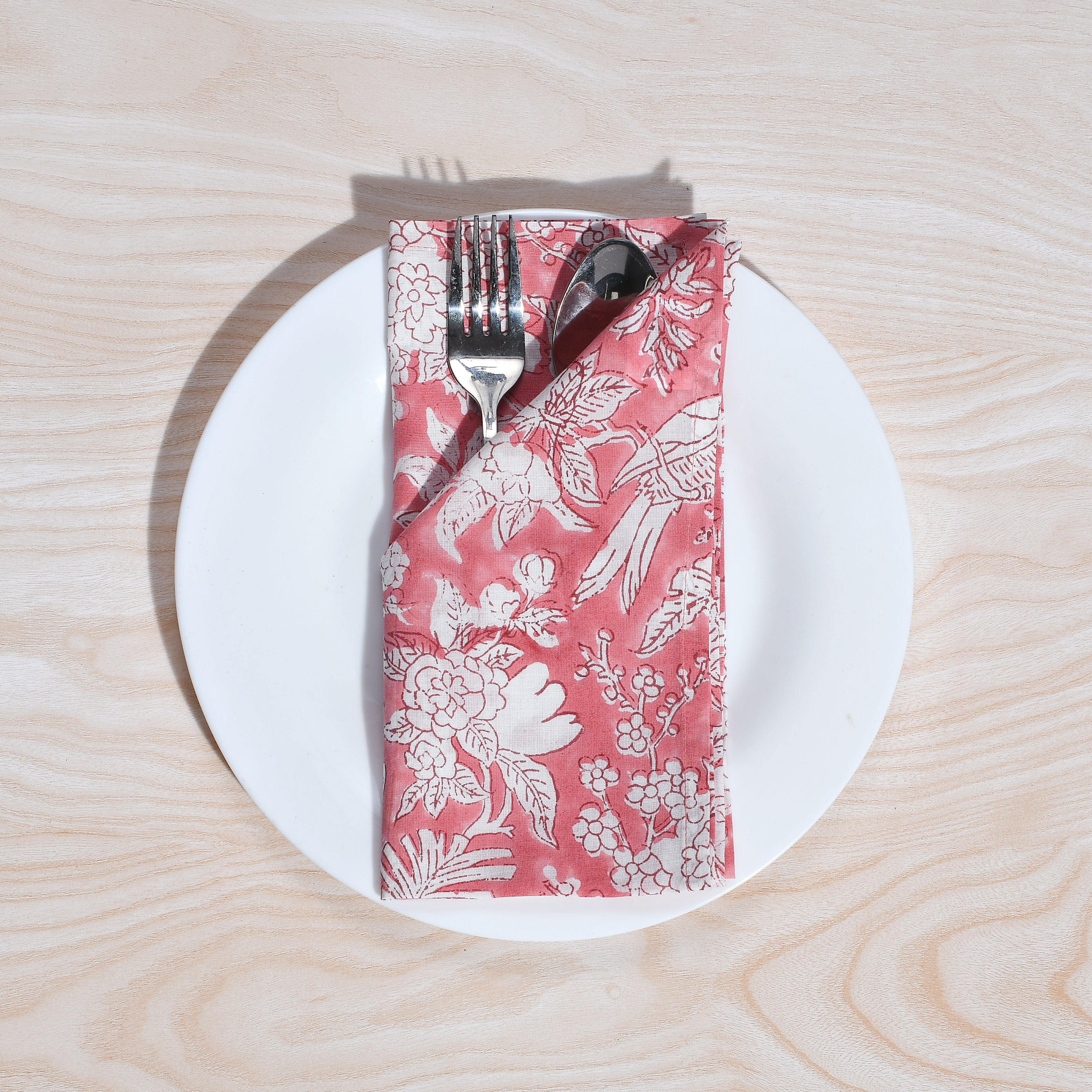 Single pink floral napkin wrapped around silverware on a white plate.