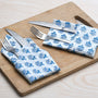 Blue floral napkin placed under silverware on wooden serving tray, with matching napkins rolled beside.

