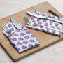 pink and white floral napkin placed under silverware on wooden serving tray, with matching napkins rolled beside.