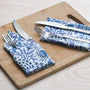 Blue floral napkin placed under silverware on wooden serving tray, with matching napkins rolled beside.
