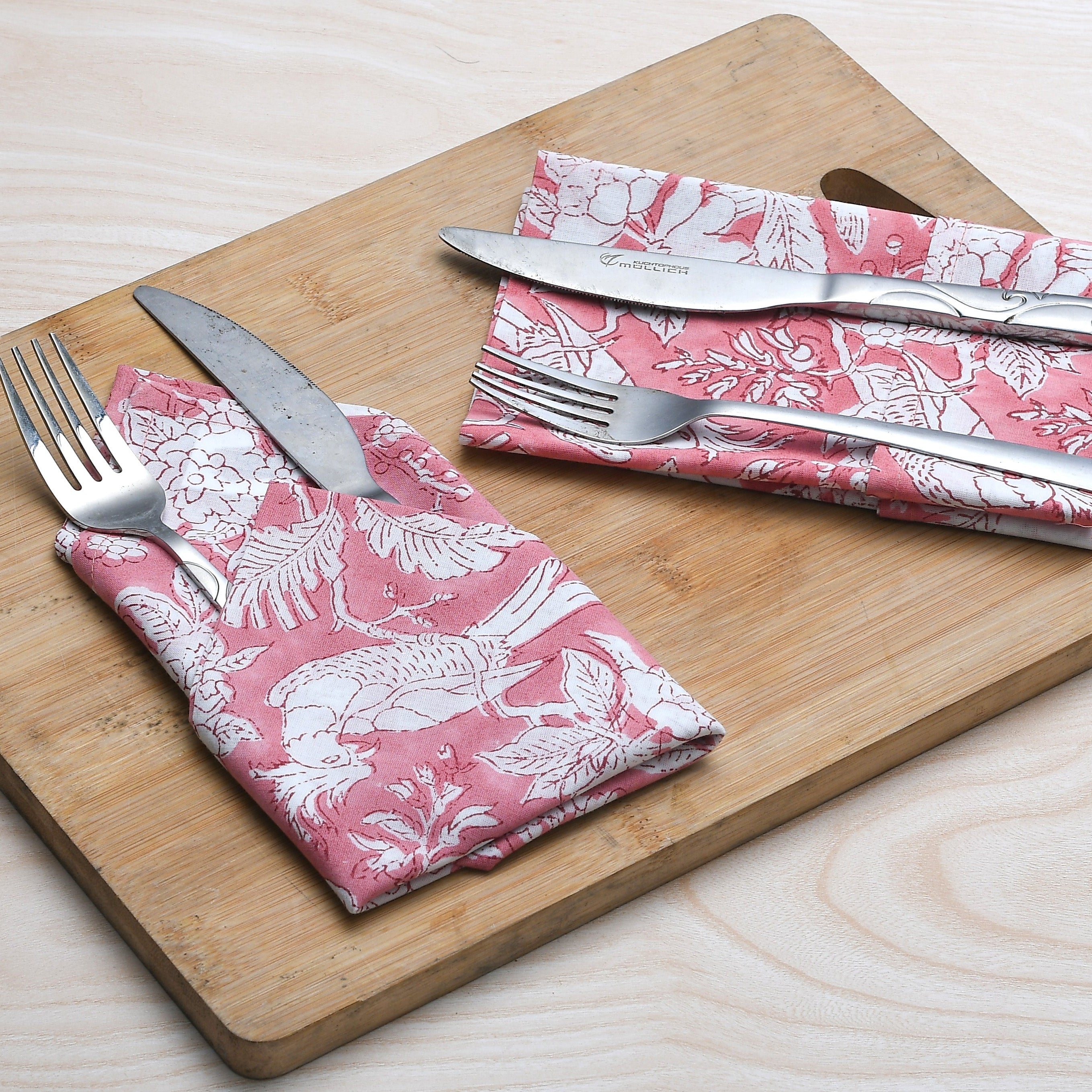 pink floral napkin placed under silverware on wooden serving tray, with matching napkins rolled beside.