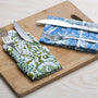 Blue and green floral napkins folded with silverware on a wooden serving tray.

