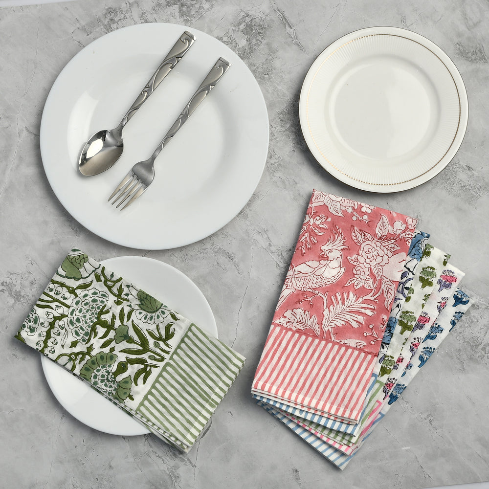 A collection of colorful cotton cloth napkins with striped border, displayed on a table alongside white plates and cutlery.