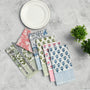 Four cotton napkins in assorted floral prints folded with silverware on a white plate.

