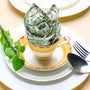 Rolled green floral napkin placed upright on a plate, styled with green leaves and silverware.