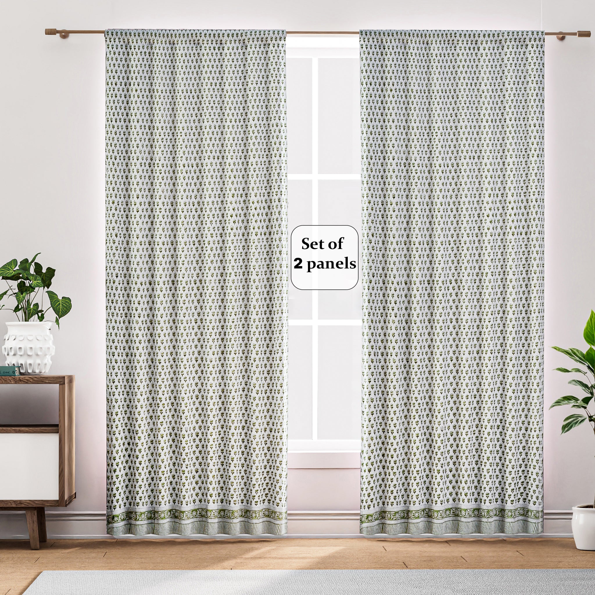 Semi-sheer cotton block print curtains in emerald green, hanging on a rod pocket, allowing natural light to filter through, with a patterned design, placed in a room with a chair and a plant.