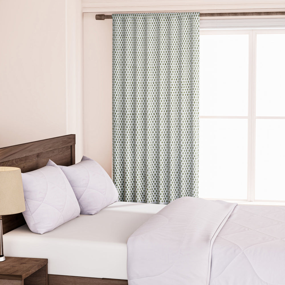 Semi-sheer cotton block print curtains in emerald green, hanging on a rod pocket, allowing natural light to filter through, with a patterned design, placed in a room with a chair and a plant.