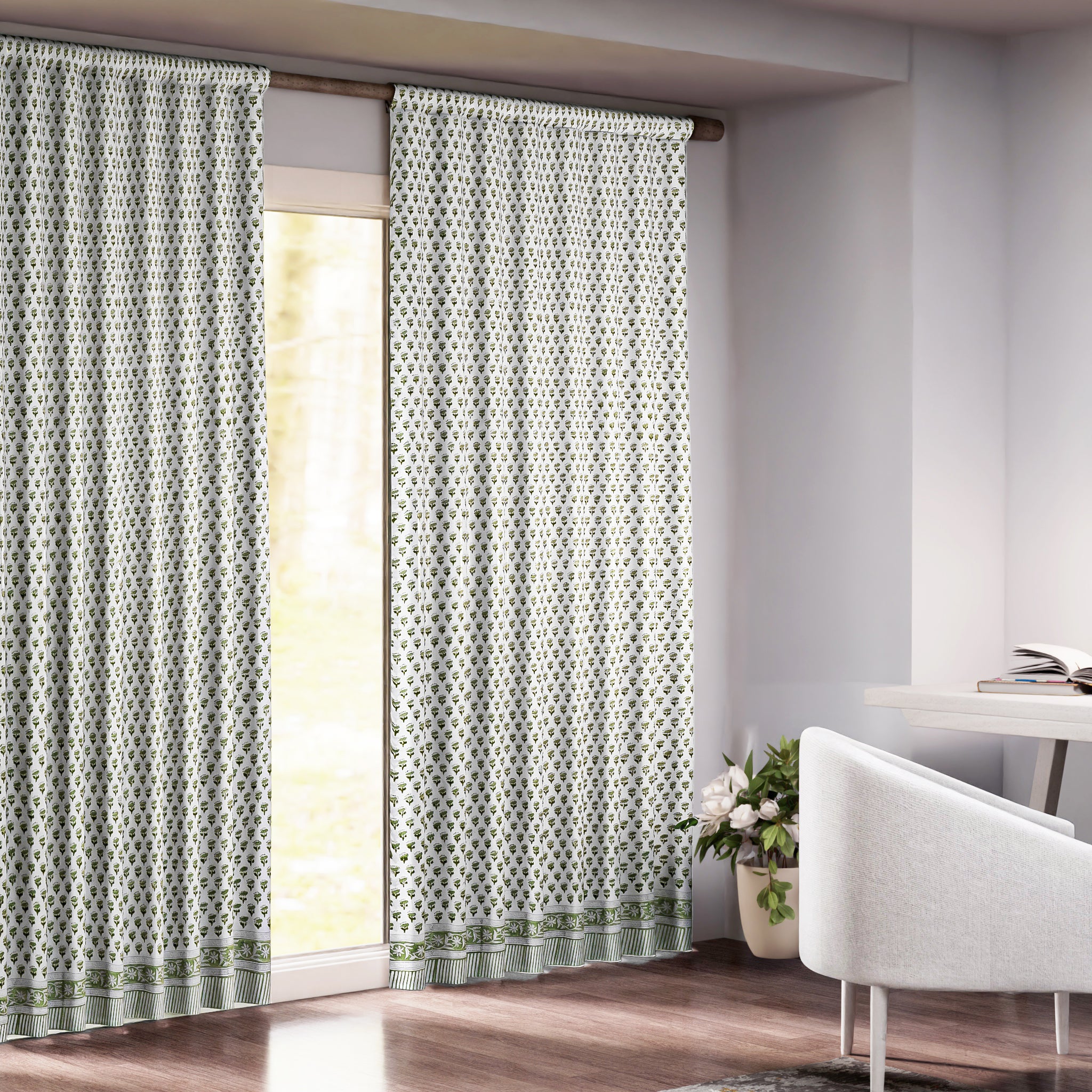 Semi-sheer cotton block print curtains in emerald green, hanging on a rod pocket, allowing natural light to filter through, with a patterned design, placed in a room with a chair and a plant.