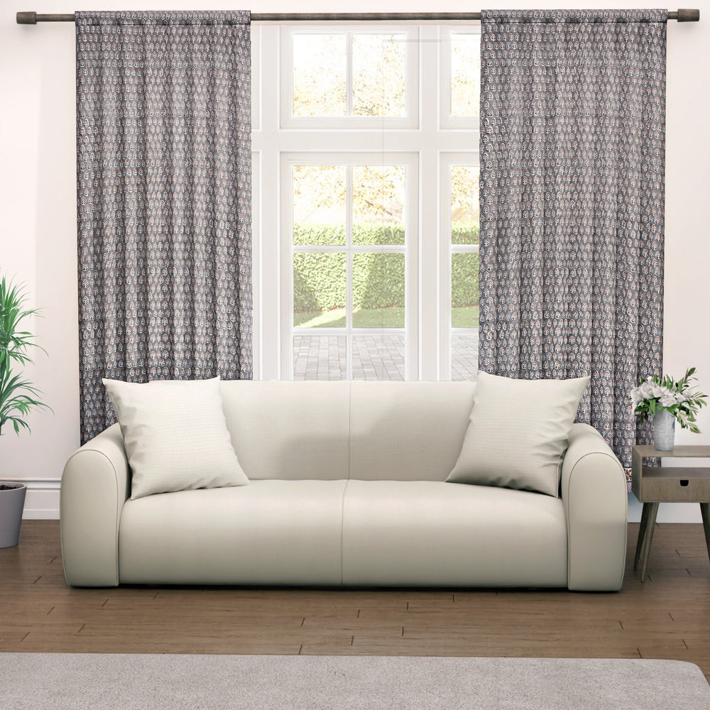 Semi-sheer cotton block print curtains in gray with intricate patterns, hanging in a room with a light source behind them, showcasing their transparent quality and rod pocket design.