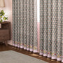 Semi-sheer cotton block print curtains in gray with intricate patterns, hanging in a room with a light source behind them, showcasing their transparent quality and rod pocket design.