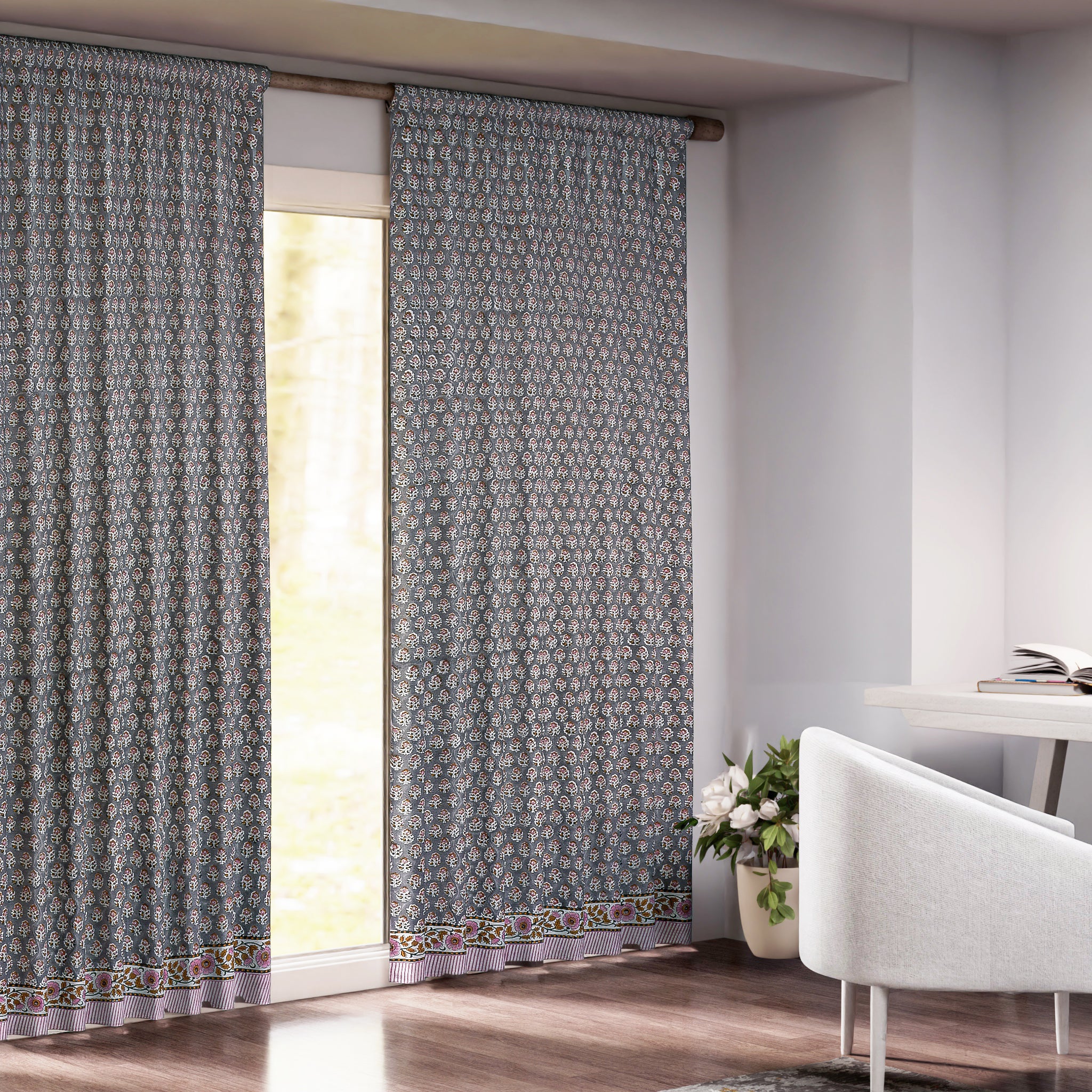 Semi-sheer cotton block print curtains in gray with intricate patterns, hanging in a room with a light source behind them, showcasing their transparent quality and rod pocket design.