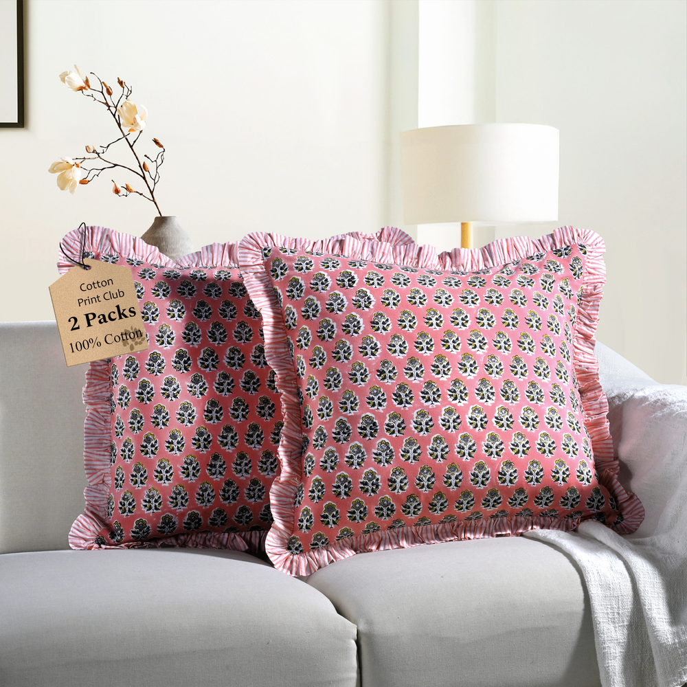 Two pink floral block print throw pillows with ruffled edges on a white sofa beside a modern lamp.