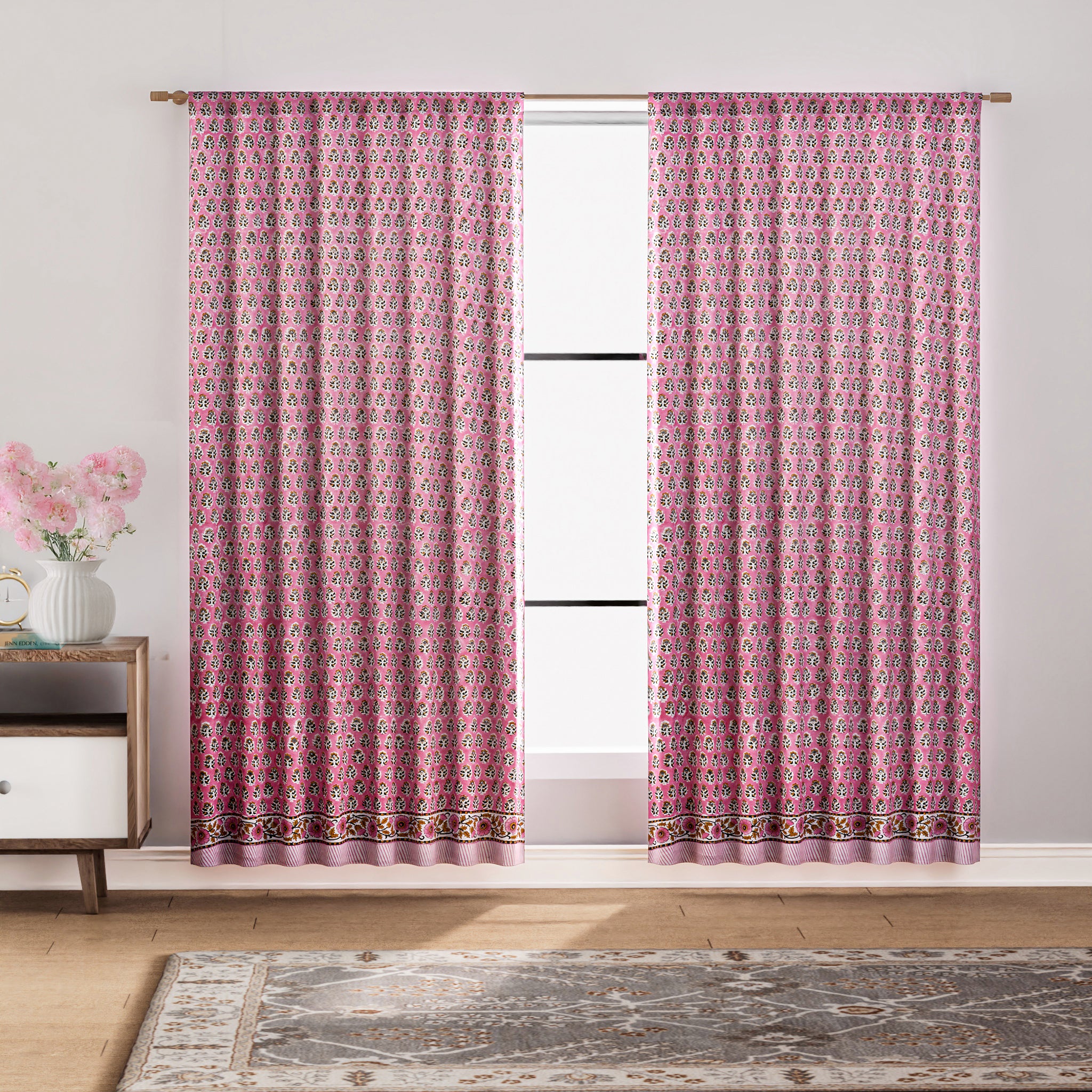 Semi-sheer cotton block print curtains in poppy pink with intricate patterns, hanging in a room with a light filtering through.