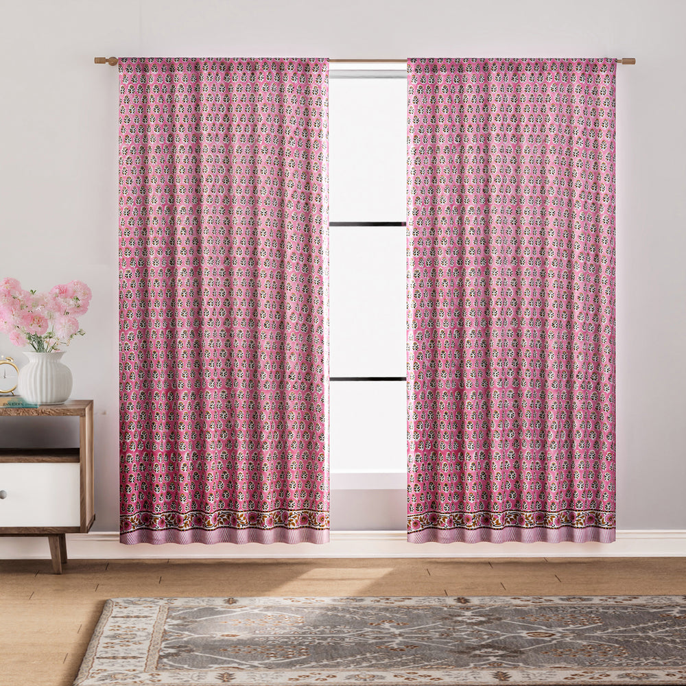 Semi-sheer cotton block print curtains in poppy pink with intricate patterns, hanging in a room with a light filtering through.