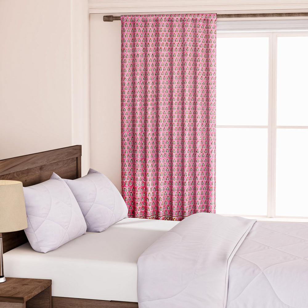Semi-sheer cotton block print curtains in poppy pink with intricate patterns, hanging in a room with a light filtering through.