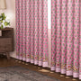 Semi-sheer cotton block print curtains in poppy pink with intricate patterns, hanging in a room with a light filtering through.