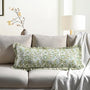A decorative pillowcase with a floral pattern and ruffle trim, in shades of green and white, displayed on a sofa.