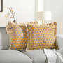 Two yellow floral block print throw pillows with ruffled edges on a white sofa beside a modern lamp